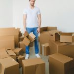 Un jeune homme pensif se tient au milieu de cartons, symbolisant un déménagement ou un changement de domicile.