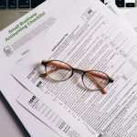 Vue aérienne de documents fiscaux et de lunettes posées sur un clavier d'ordinateur portable, idéale pour des thèmes financiers ou comptables.