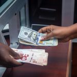 Hands exchanging US and local currency at a bank counter, signifying international finance. Des mains échangeant de la monnaie américaine et locale à un guichet bancaire, signifiant la finance internationale.
