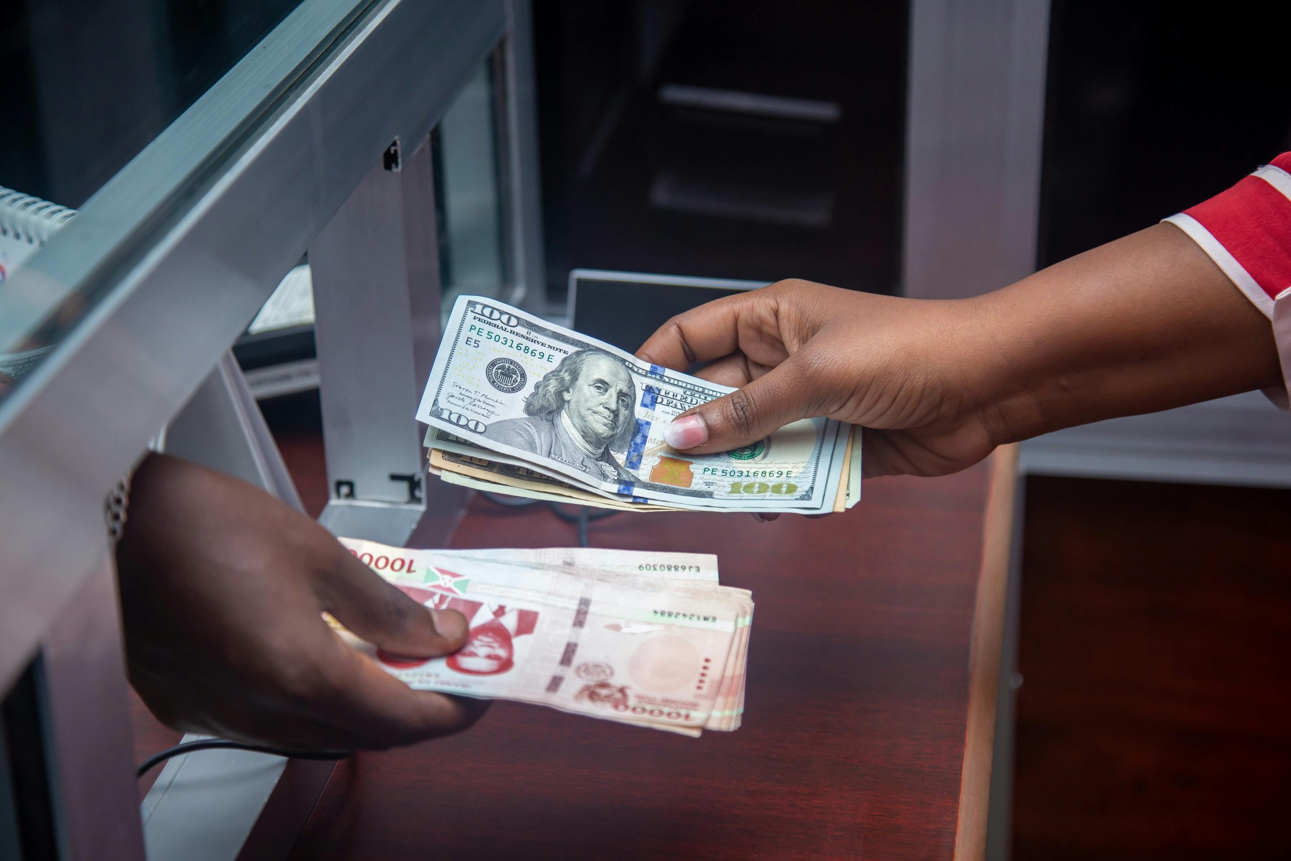 Hands exchanging US and local currency at a bank counter, signifying international finance. Des mains échangeant de la monnaie américaine et locale à un guichet bancaire, signifiant la finance internationale.