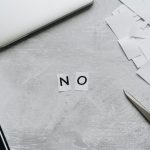 Top view of scattered paper squares, laptop, and scissors forming the word 'NO', implying rejection or denial. Vue de dessus de carrés de papier dispersés, d'un ordinateur portable et de ciseaux formant le mot « NON », impliquant un rejet ou un refus.
