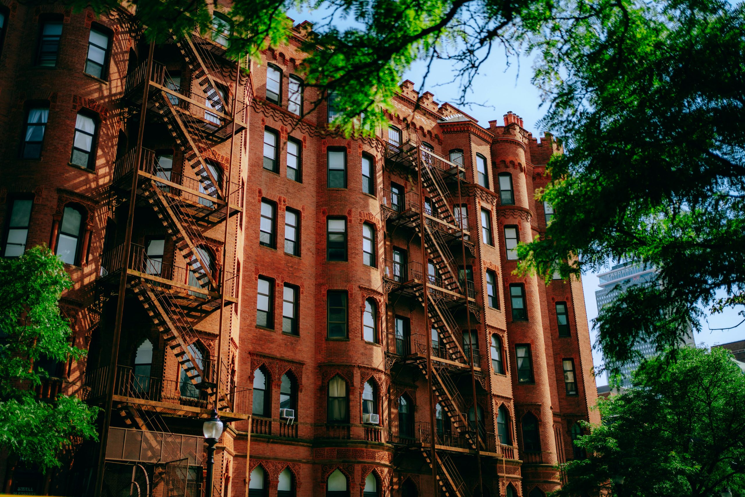 Traditional red brick building with metal fire escapes in an urban setting. Bâtiment en brique rouge traditionnel avec escaliers de secours métalliques en milieu urbain.