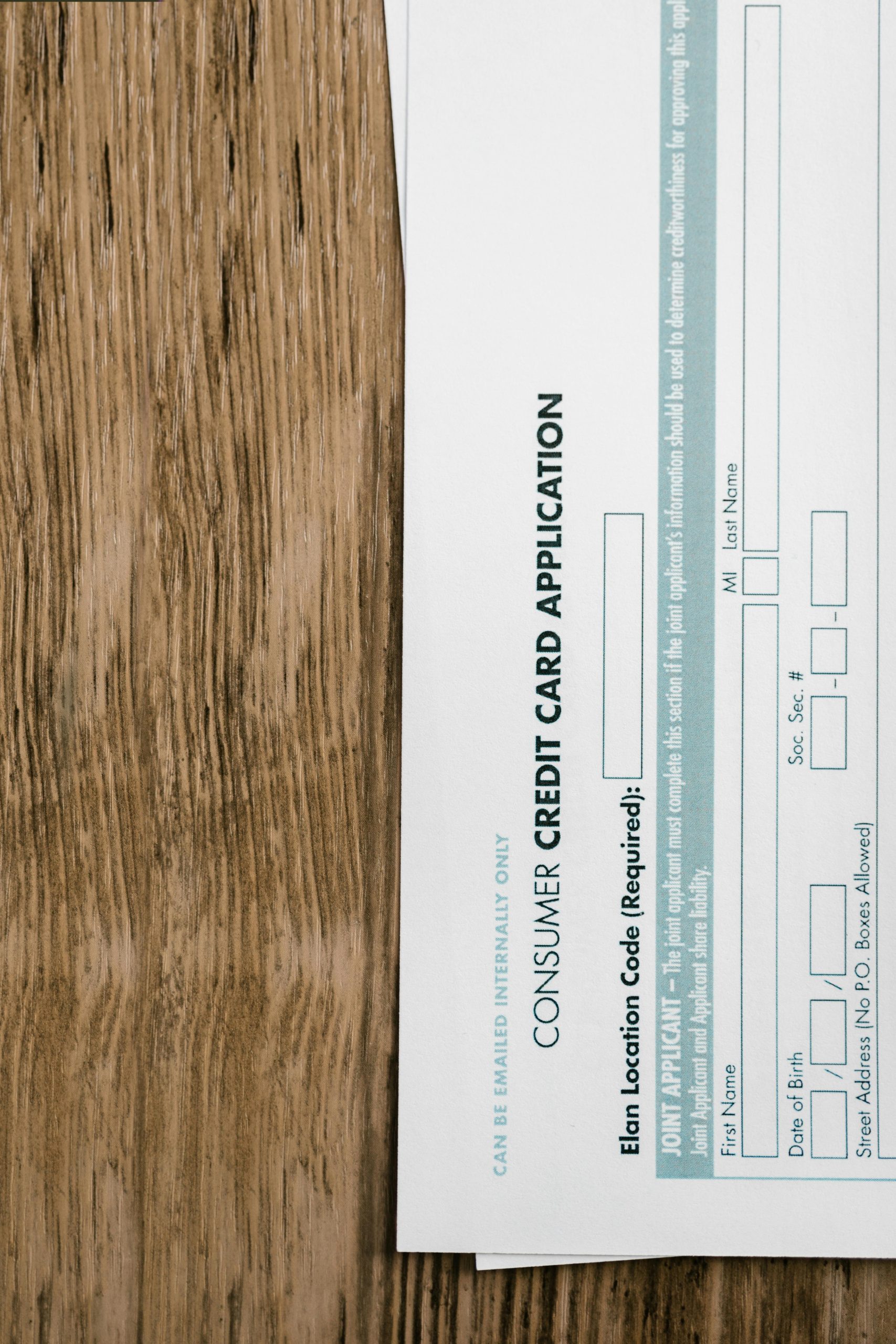 Close-up of a consumer credit card application form on a wooden surface, indicating financial paperwork. Gros plan sur un formulaire de demande de carte de crédit à la consommation sur une surface en bois, indiquant des documents financiers.