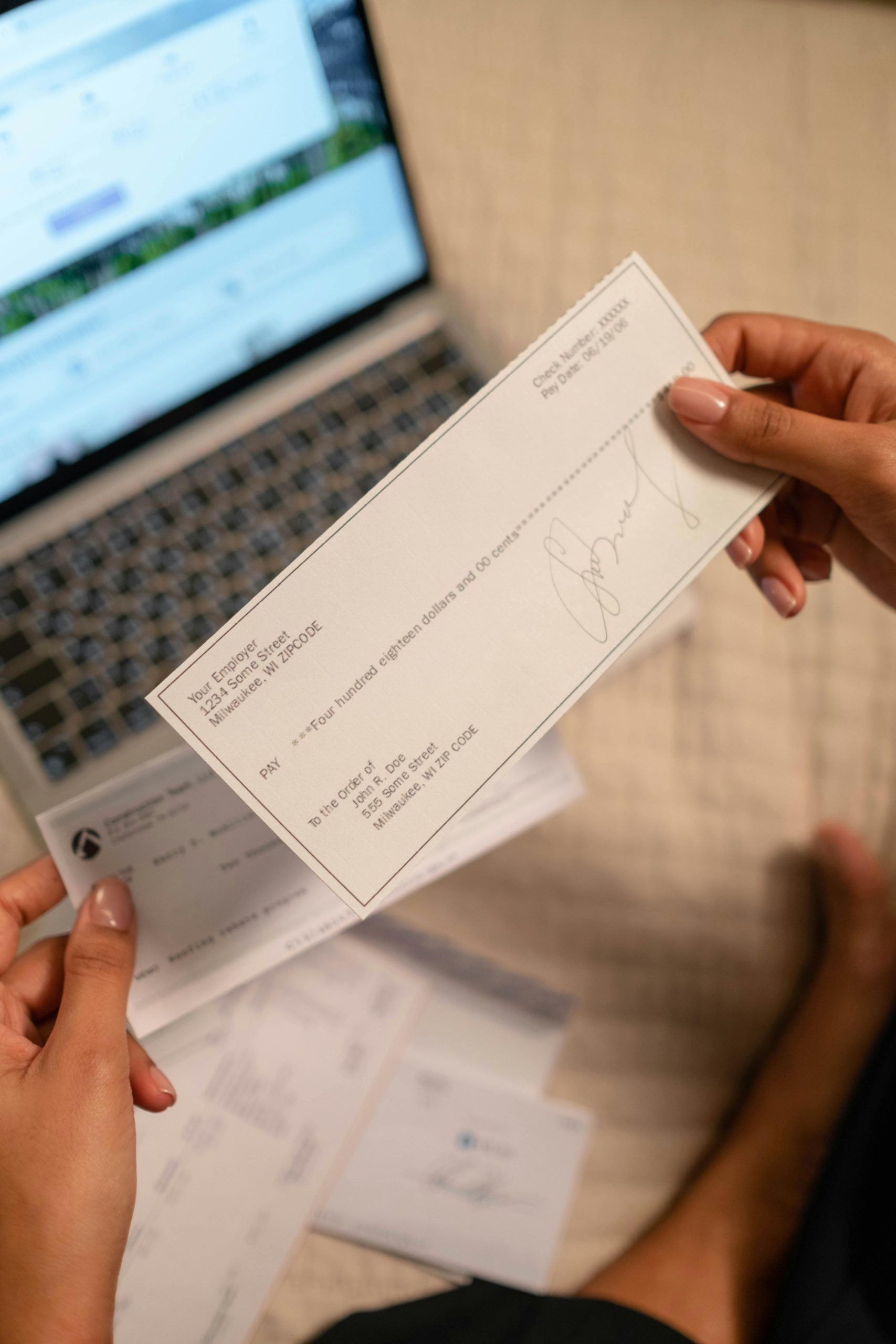 Individual holding a cheque over laptop, signifying online banking or financial transaction. Une personne tenant un chèque au-dessus d'un ordinateur portable, symbolisant les services bancaires en ligne ou une transaction financière.