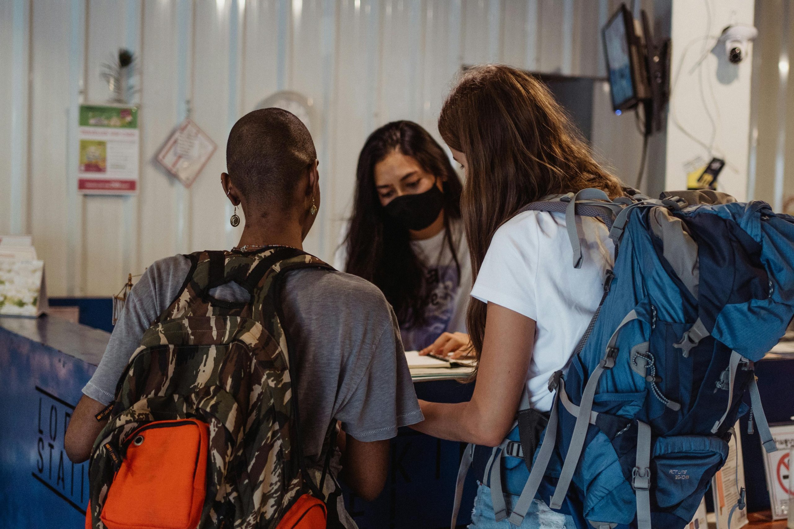 Two travelers with backpacks check in at a hostel reception counter. Deux voyageurs avec des sacs à dos font l'enregistrement à la réception d'une auberge.
